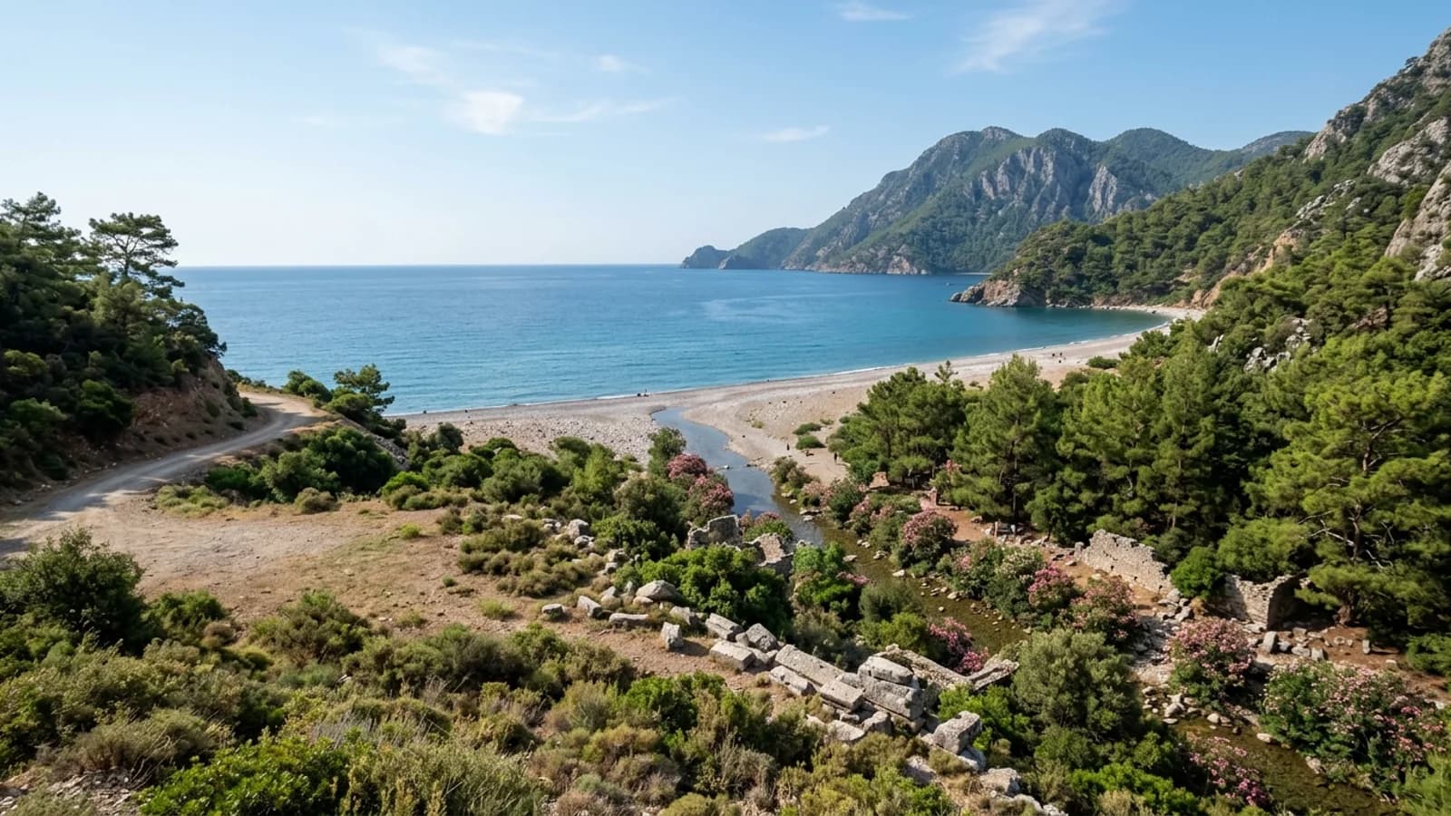 Une vallée fluviale boisée avec des ruines mène à la plage de galets d'Olympos, accessible via taxi transfert Kemer.