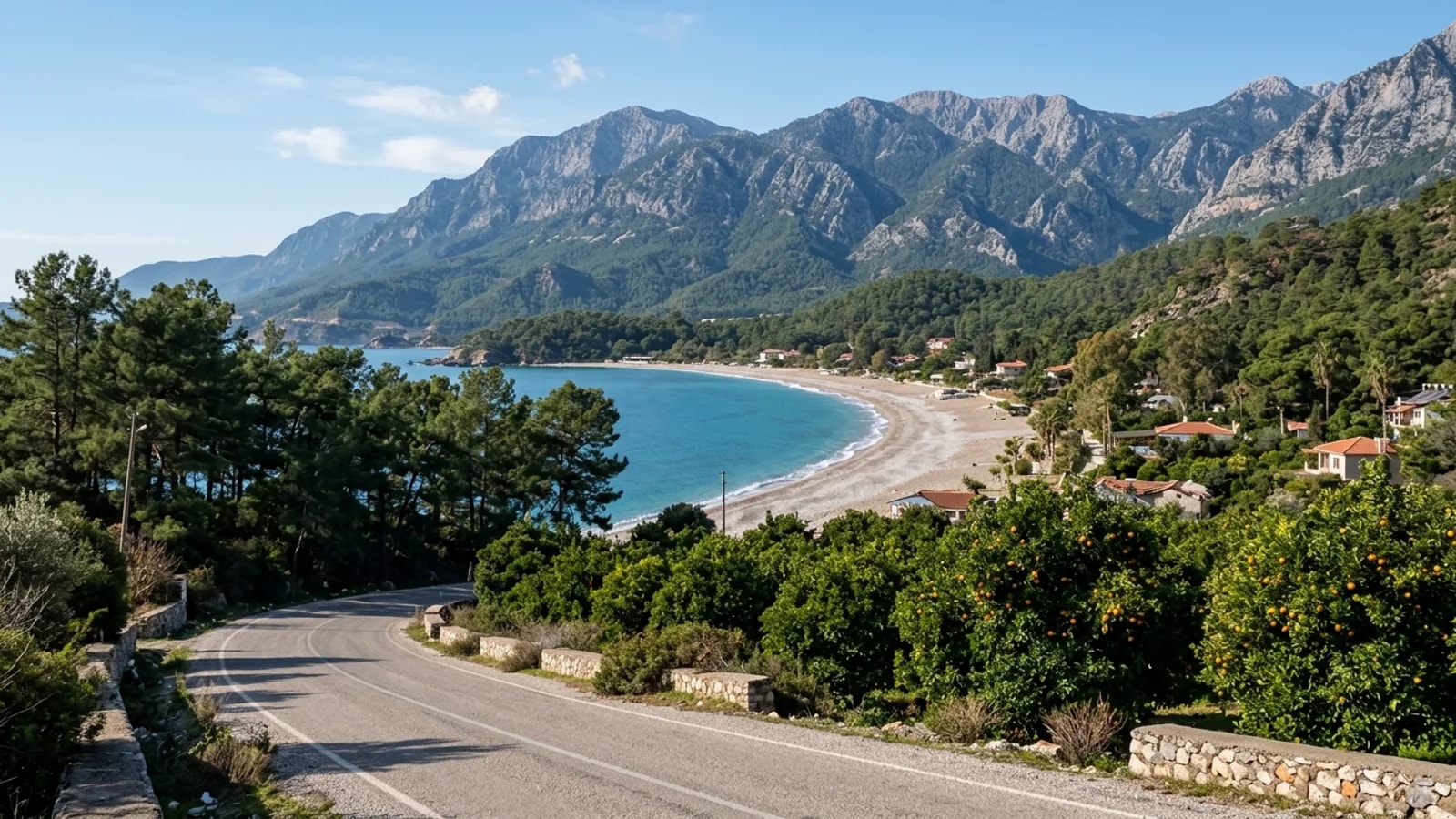 Un transfert Çamyuva dévoile une crique de galets, des orangeraies, une route de village et la chaîne des Beydaglari en arrière-plan.